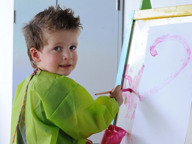 Boy in art smock smiling and painting on canvas