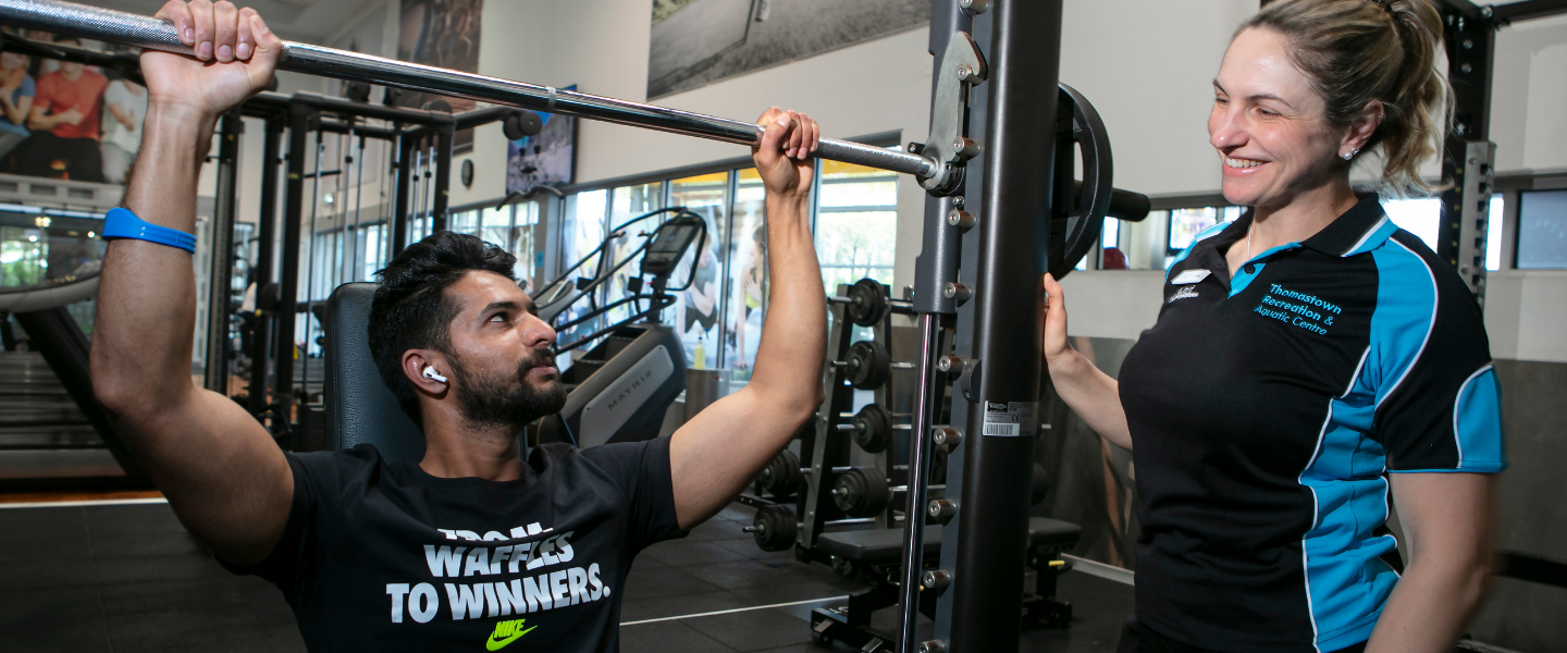 Man using weights in gym with personal trainer guidance