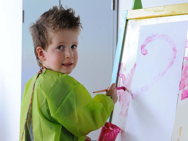 Boy in art smock smiling and painting on canvas