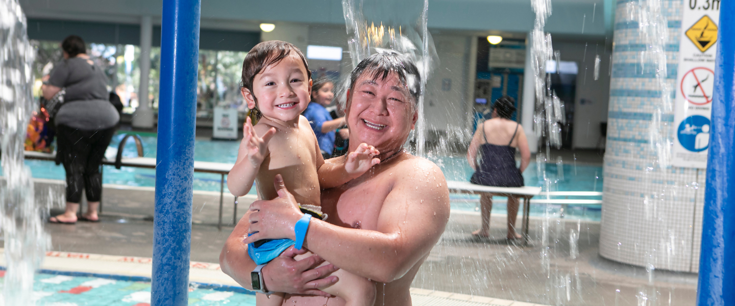 Father and young son in leisure pool under water feature