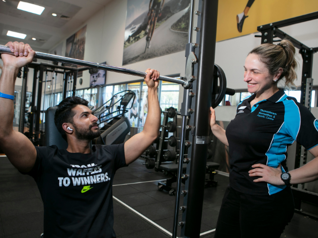 Gym instructor assisting man with gym equipment